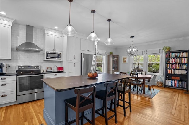 kitchen featuring stainless steel appliances, wall chimney range hood, dark countertops, backsplash, and crown molding