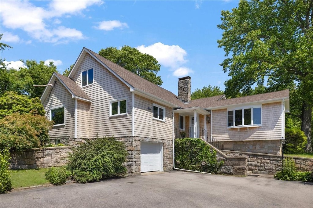 39 Highland Ave, Narragansett, RI 02882 - view of front of house featuring a chimney, an attached garage, asphalt driveway, stone siding, and roof with shingles