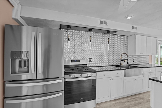 kitchen with appliances with stainless steel finishes, dark countertops, white cabinets, a sink, and light wood-style flooring