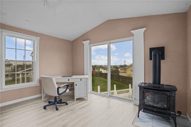 office with light wood finished floors, vaulted ceiling, plenty of natural light, and a wood stove