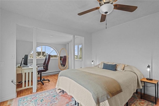 bedroom featuring wood finished floors, an office area, baseboard heating, ceiling fan, and baseboards