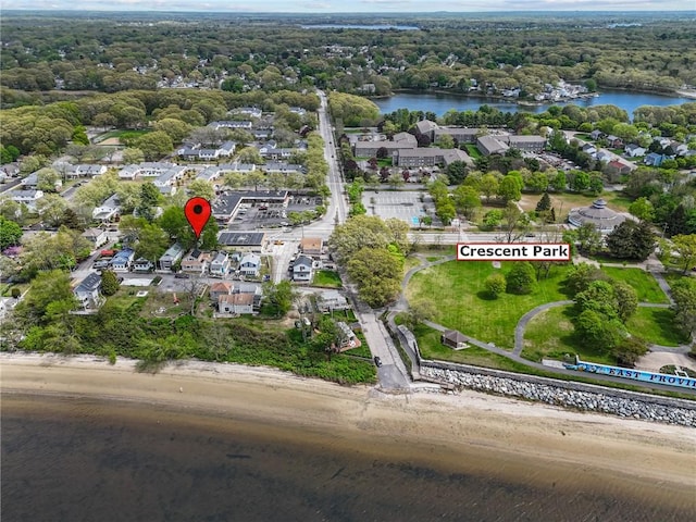aerial view of property and surrounding area featuring a nearby body of water, nearby suburban area, and a heavily wooded area