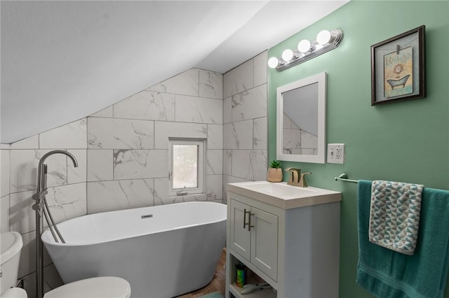 bathroom featuring toilet, vanity, a freestanding tub, tile walls, and vaulted ceiling