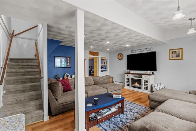 living area with wood finished floors, a baseboard heating unit, stairs, recessed lighting, and a lit fireplace