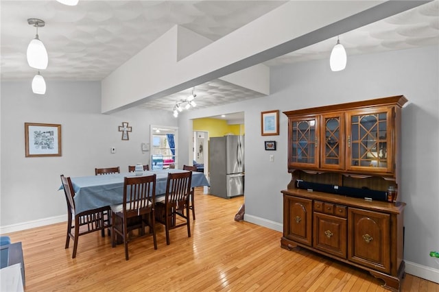 dining area featuring light wood-style flooring, baseboards, and beamed ceiling
