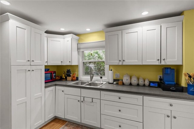 kitchen with a sink, white cabinetry, dark countertops, recessed lighting, and light wood-style floors