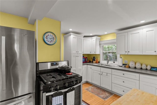 kitchen with appliances with stainless steel finishes, a sink, white cabinets, light wood finished floors, and recessed lighting