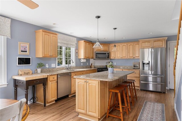 kitchen featuring stainless steel appliances, a sink, a center island, wood finished floors, and a kitchen bar