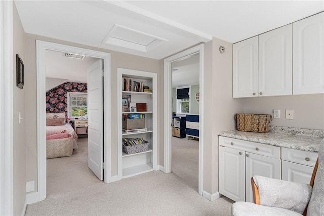 corridor featuring light carpet, attic access, baseboards, and built in shelves