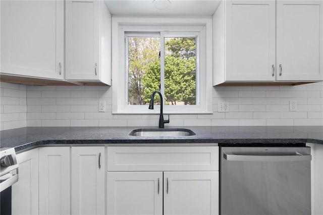 kitchen featuring stainless steel appliances, a sink, white cabinetry, dark stone countertops, and backsplash