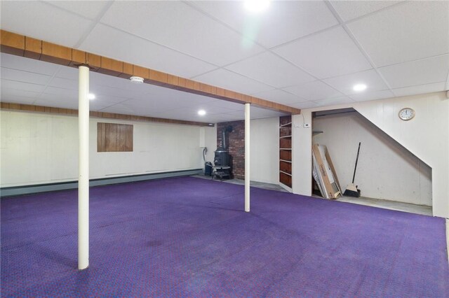 finished below grade area with carpet floors, a wood stove, a drop ceiling, baseboard heating, and recessed lighting