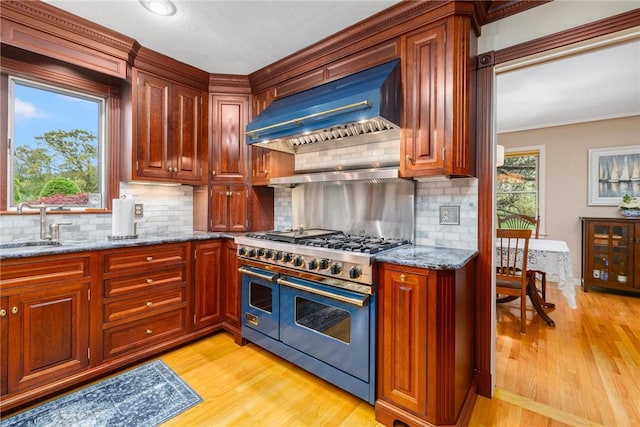 831 N Quidnessett Rd, North Kingstown, RI 02852 - kitchen with range with two ovens, wall chimney exhaust hood, a sink, light stone counters, and light wood-style flooring