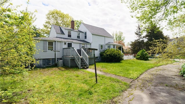 back of property with a chimney, a shingled roof, a yard, and a wooden deck