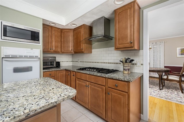 218 Burnt Cedar Dr, North Kingstown, RI 02852 - kitchen with stainless steel appliances, crown molding, wall chimney range hood, light stone counters, and brown cabinetry