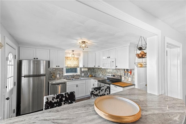 kitchen featuring stainless steel appliances, a sink, white cabinets, tasteful backsplash, and light stone counters