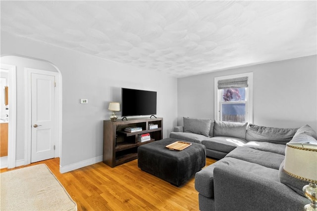 living area with arched walkways, light wood-style floors, and baseboards