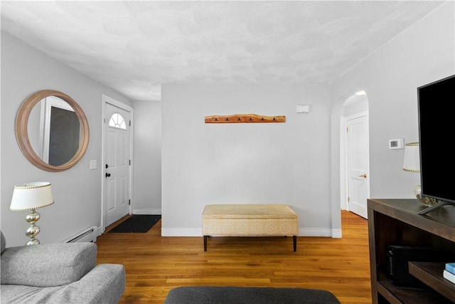living area featuring baseboard heating, arched walkways, wood finished floors, and baseboards