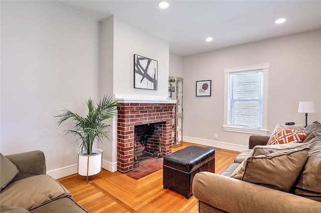 living area featuring baseboards, recessed lighting, a brick fireplace, and light wood-style flooring