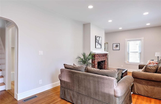living area with arched walkways, light wood-style flooring, a fireplace, baseboards, and recessed lighting
