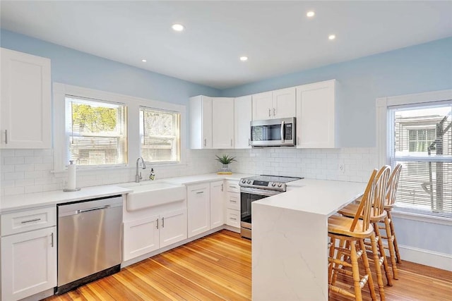 kitchen with stainless steel appliances, a sink, light wood-style flooring, a kitchen bar, and healthy amount of natural light