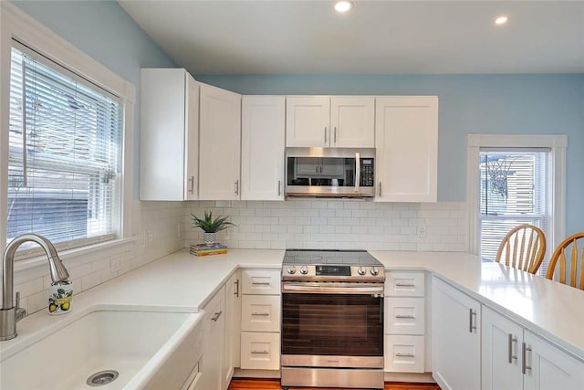 kitchen featuring stainless steel appliances, a sink, white cabinets, decorative backsplash, and light countertops