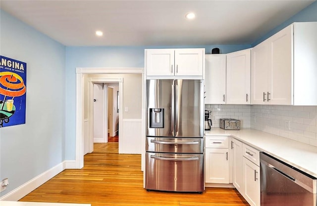 kitchen with appliances with stainless steel finishes, light countertops, white cabinetry, light wood-type flooring, and decorative backsplash