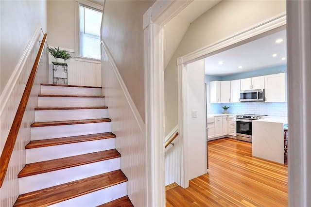 stairway with wood finished floors, a wainscoted wall, and recessed lighting