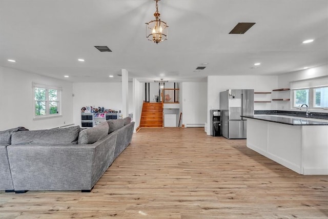 living area featuring baseboard heating, healthy amount of natural light, stairs, light wood finished floors, and recessed lighting