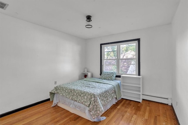 bedroom with a baseboard radiator, wood finished floors, and baseboards