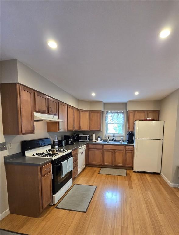 94 Barton St, Pawtucket, RI 02860 - kitchen with white appliances, under cabinet range hood, a sink, dark countertops, and brown cabinets