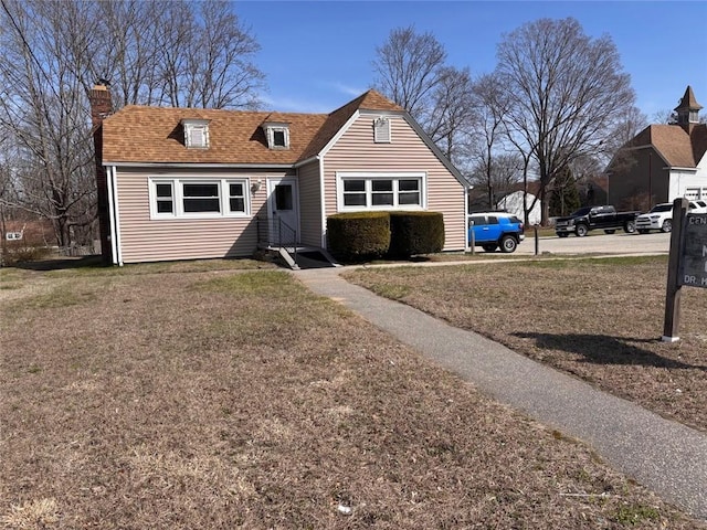 view of front facade featuring a front yard, a chimney, and a shingled roof