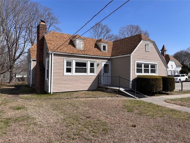 rear view of house featuring a chimney, a yard, and a shingled roof