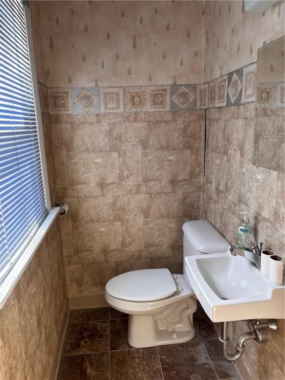 half bath featuring tile walls, toilet, a sink, and wallpapered walls