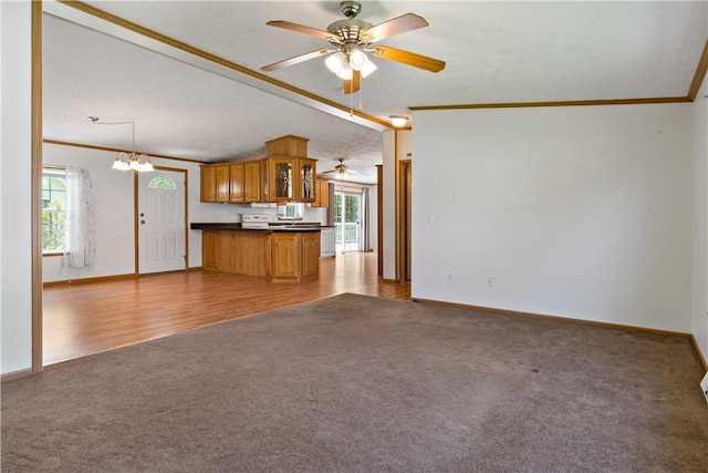 unfurnished living room with light carpet, crown molding, ceiling fan, baseboards, and a chandelier