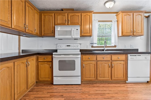 kitchen featuring white appliances, a sink, light wood-type flooring, dark countertops, and brown cabinetry