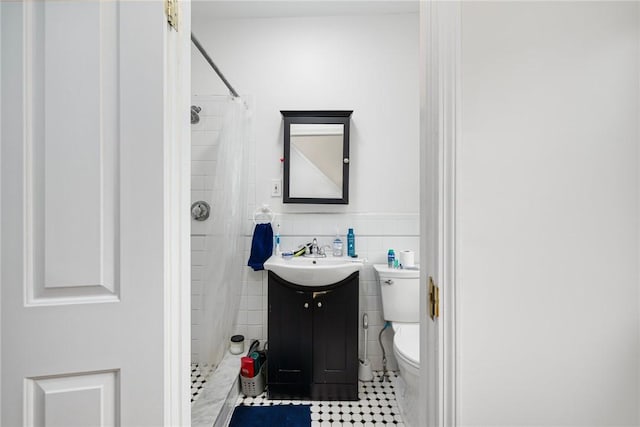 bathroom with a stall shower, toilet, tile patterned floors, vanity, and wainscoting