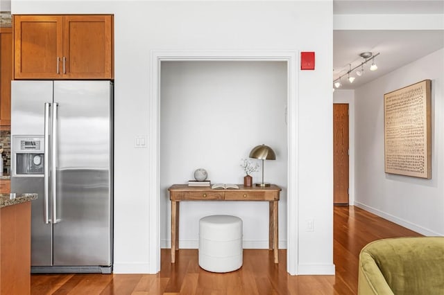 kitchen with high end refrigerator, wood finished floors, stone countertops, brown cabinetry, and baseboards