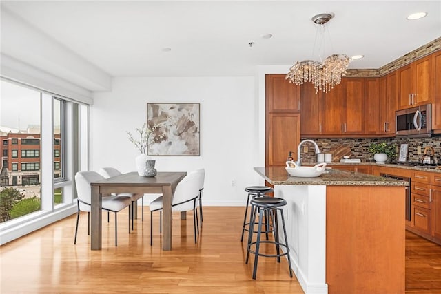 kitchen with stainless steel appliances, dark stone countertops, a breakfast bar area, a chandelier, and brown cabinetry