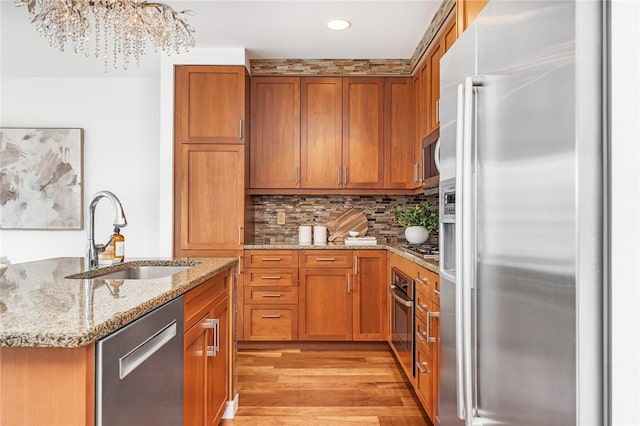 kitchen with stainless steel appliances, a sink, brown cabinetry, light wood-style floors, and light stone counters