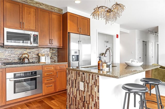 kitchen featuring appliances with stainless steel finishes, wood finished floors, a sink, a kitchen breakfast bar, and a chandelier