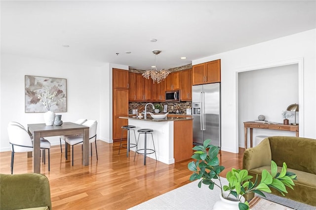 kitchen featuring appliances with stainless steel finishes, open floor plan, a chandelier, light wood finished floors, and a breakfast bar