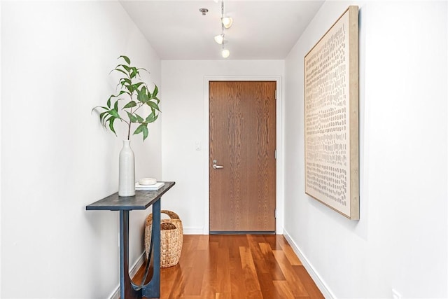 doorway to outside with wood finished floors, track lighting, and baseboards