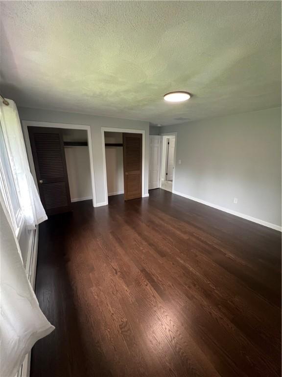 446 Angell Rd, North Providence, RI 02904 - unfurnished bedroom featuring baseboards, a textured ceiling, dark wood-type flooring, and two closets
