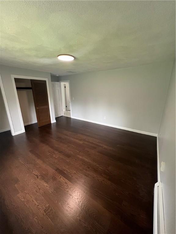 446 Angell Rd, North Providence, RI 02904 - unfurnished bedroom with a baseboard radiator, baseboards, dark wood-style flooring, and a textured ceiling