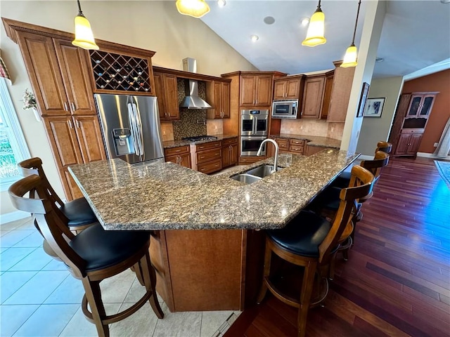kitchen with stainless steel appliances, wall chimney range hood, a sink, brown cabinets, and a kitchen breakfast bar