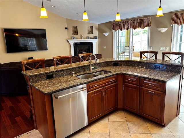 kitchen featuring stainless steel dishwasher, a sink, open floor plan, an island with sink, and pendant lighting