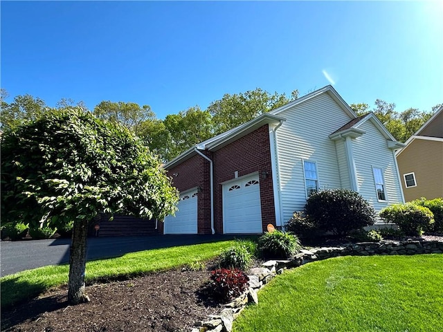 view of home's exterior featuring an attached garage, a yard, driveway, and brick siding