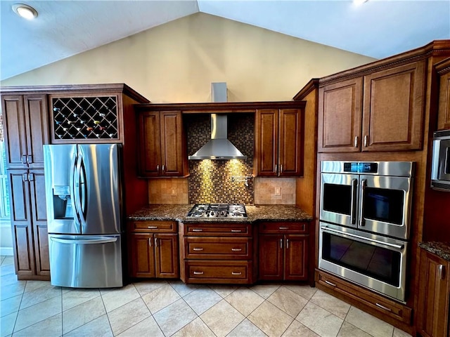 kitchen with appliances with stainless steel finishes, wall chimney range hood, vaulted ceiling, decorative backsplash, and light tile patterned flooring