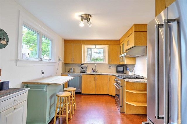 kitchen with high quality appliances, under cabinet range hood, plenty of natural light, and wood finished floors
