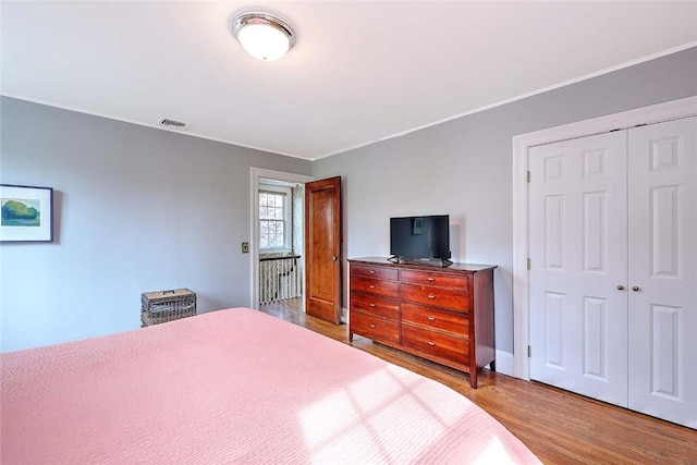 bedroom with wood finished floors, a closet, crown molding, and baseboards